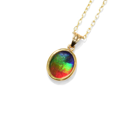 This ammolite pendant is oval in shape and has a triangular bail. The colours of the ammolite include violet, dark blue, green, lime green, orange, and red.