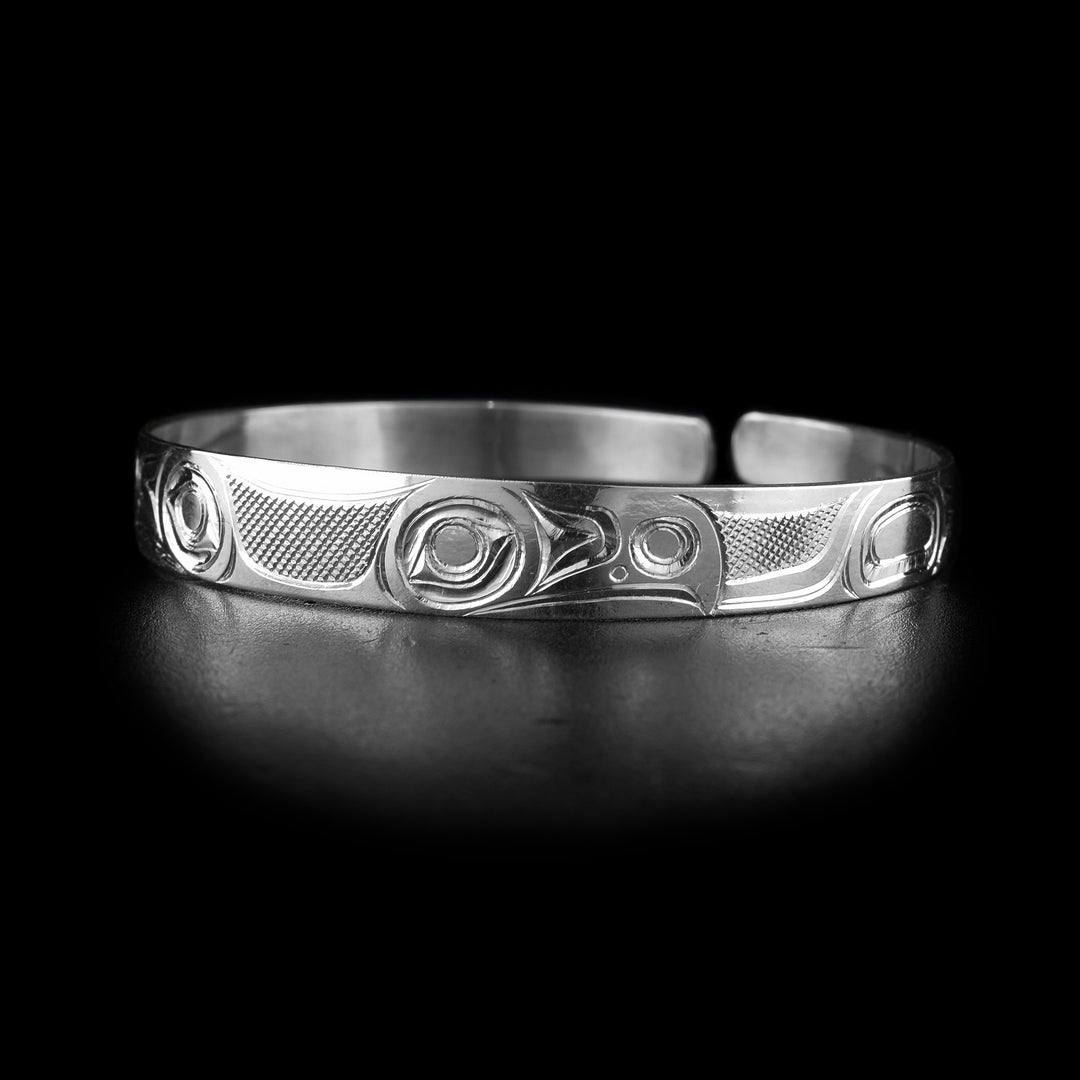 This Eagle cuff bracelet has a single, thin band with a gap in the back. The band is made from sterling silver and there are tow depictions of the Eagle carved into it. There are two eagle heads at the top of the band facing away from each other. There are wing details on the ends of the band.