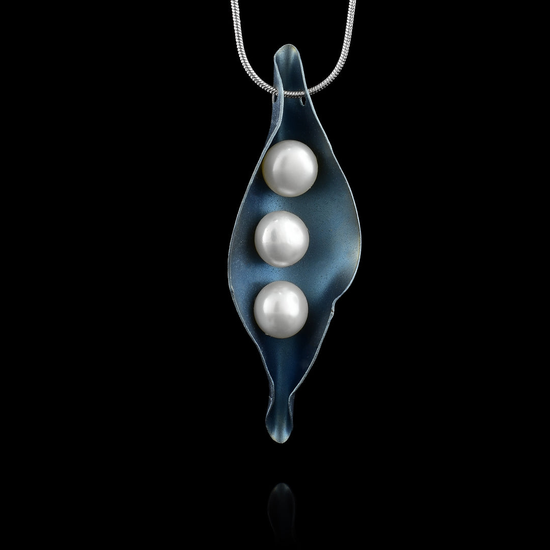 This pearl drop pendant necklace is made from a long, oval shaped piece of blue titanium. The titanium represents a pea pod and is curved up with three white pearls that represent the peas.