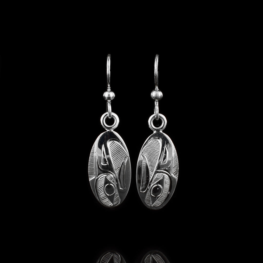 These earrings Eagle have long, oval shaped hangs made from sterling silver. There are carvings on the hangs depicting the head of the Eagle at a side profile. The Eagle is looking upwards and its beak is open. There are cross hatching designs in the background of the scene.