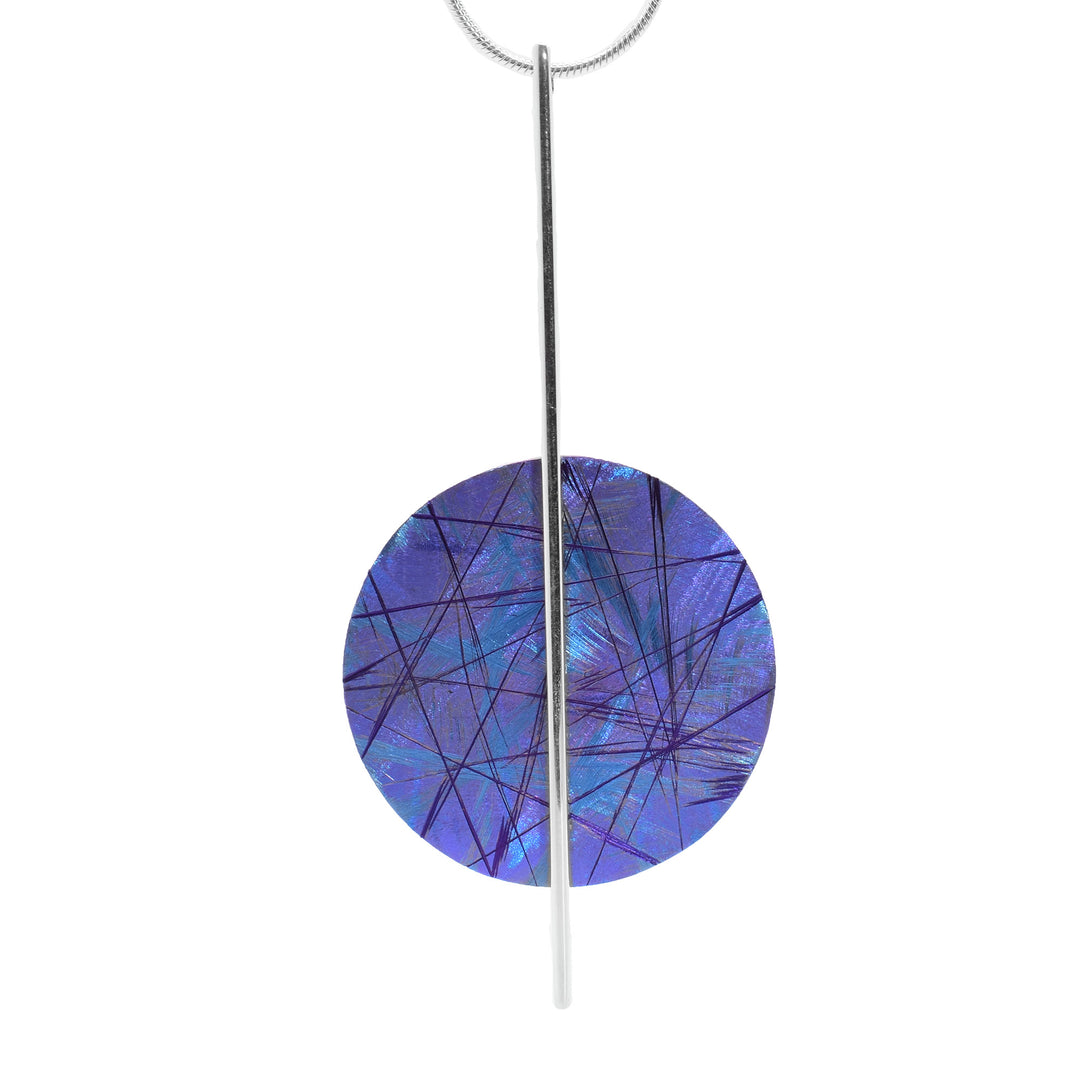 This long circle pendant necklace has a sterling silver wire that drops down and has a titanium circle attached to it with purple and blue designs across its surface. The colors and patterns are achieved by anodizing the material.