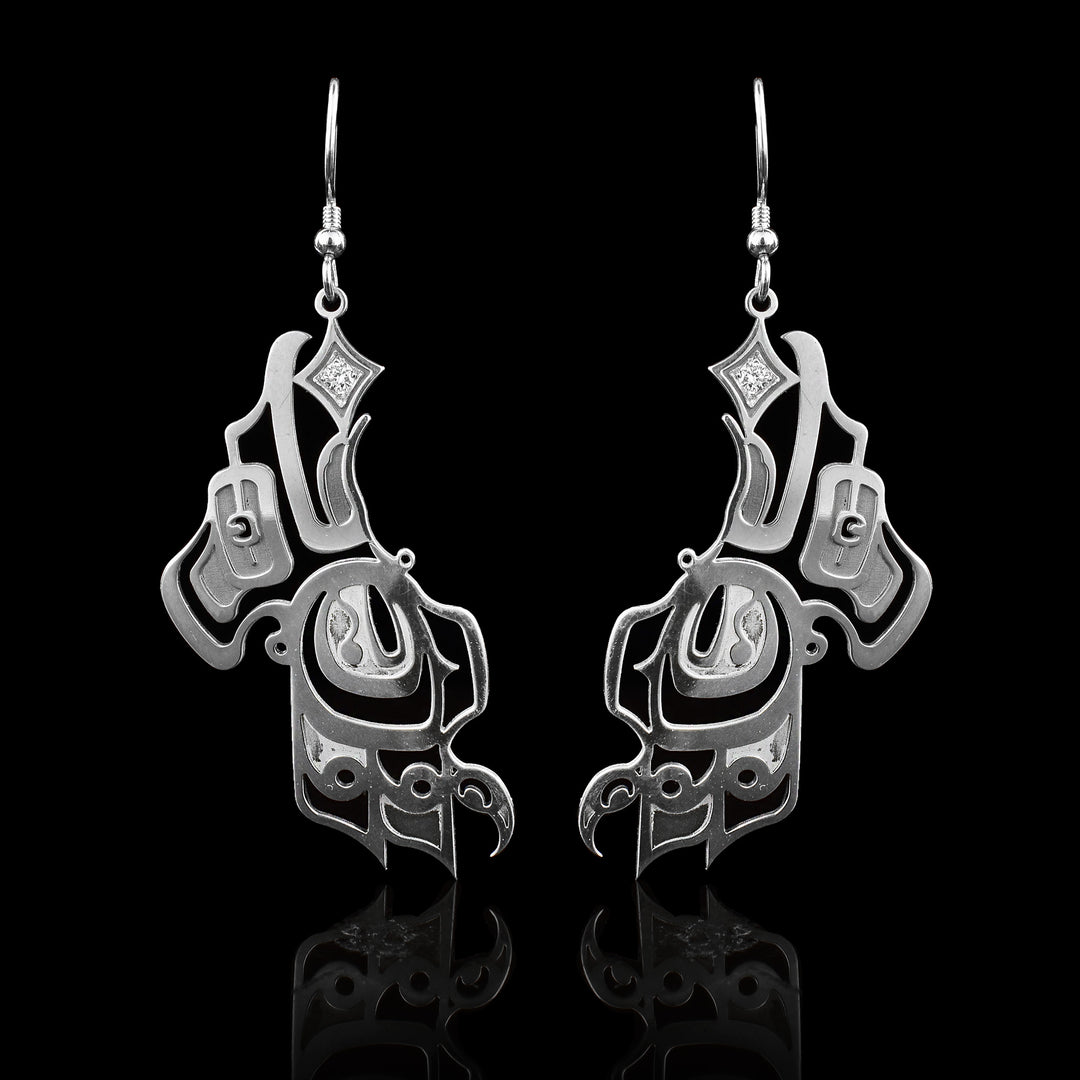 These sterling silver diamond dangle earrings are shaped like the side profile of the Raven with its wing facing down and its head straight up. There are cutout designs detailing the legend and there is a diamond held in its beak with a star shape.