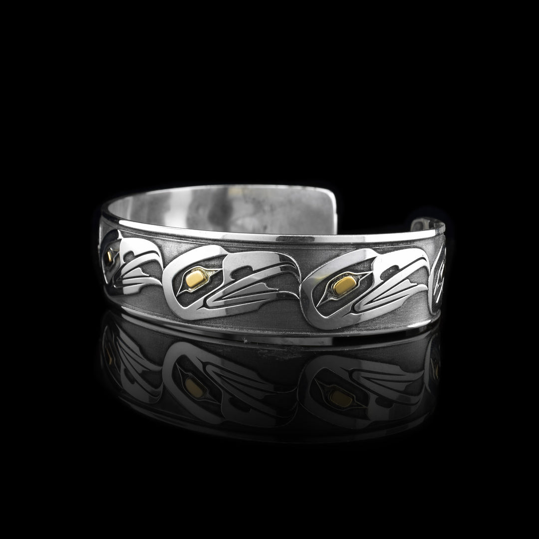 This striking eagle cuff bracelet is handcrafted from sterling silver and features inlaid 14k gold eyes. Showcasing a bold and elegant design, the eagle cuff bracelet highlights the form of an eagle in a traditional style, with flowing lines and intricate detailing. The combination of polished silver and gold accents adds depth and contrast.