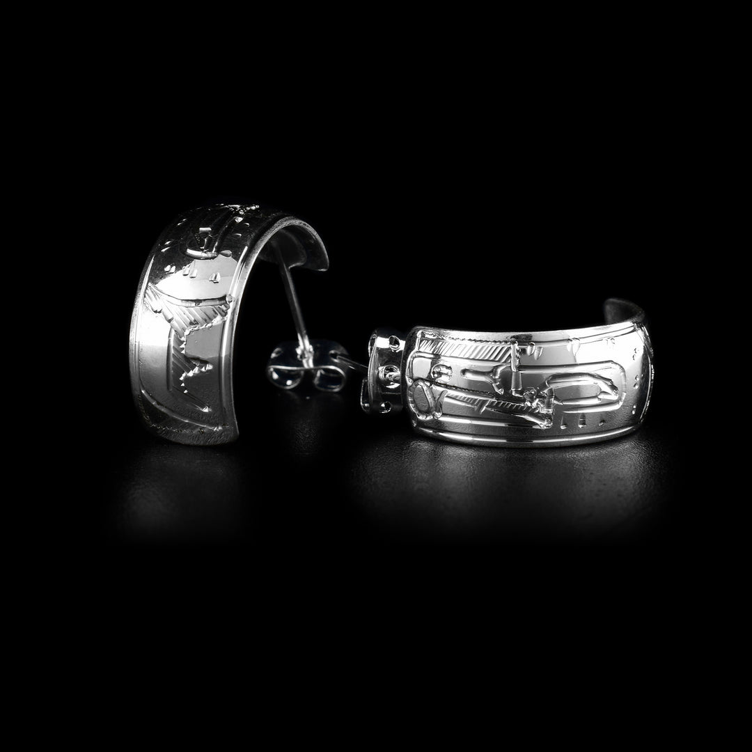 These wide hoop earrings are made from sterling silver and have wide bands curved into half hoop stud earrings. The head of the Raven is carved into the bands with its beak facing the studs and there is a wing detail behind the head.