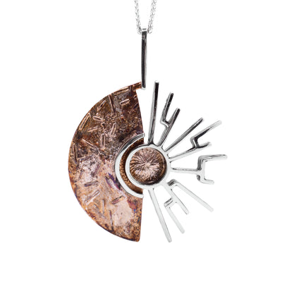 This oxidized silver necklace is in the shape of a half circle on the left and has multiple sterling silver accents in the shape of the sun's rays on the right. It is light and dark brown in colour with a long, linear bail.