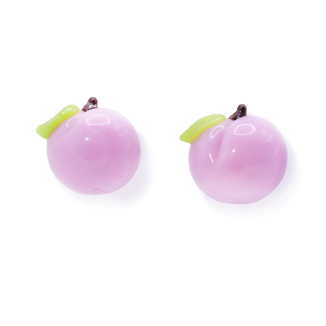 These peach earrings studs are made from lampworked glass and are shaped like peaches. There is round, light pink glass with a crease in the center of it. There is a green leaf and brown stem at the top of the studs.