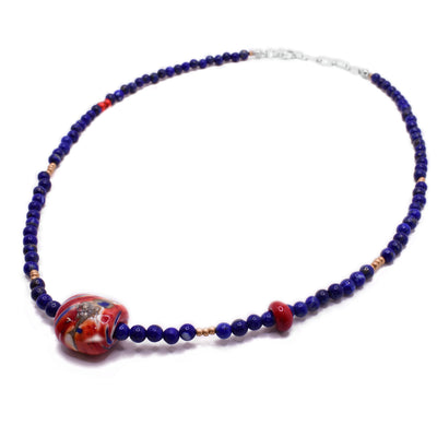 This lapis bead necklace is made from tiny lapis beads making up the entirety of the necklace with other coloured glass accents throughout. There is a large red and blue glass bead in the center.