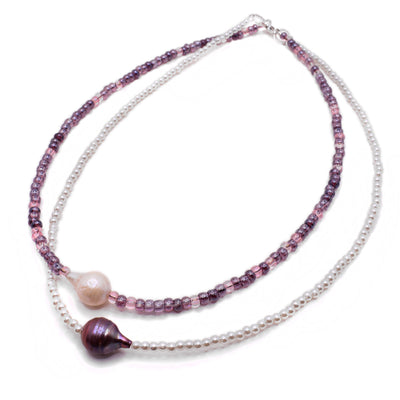 This freshwater pearl necklace is layered with the first layer having a white pearl as the centerpiece and pink and purple beads making the rest of the necklace. The second layer has a dark purple pearl as the centerpiece and white glass beads making up the rest of the necklace.