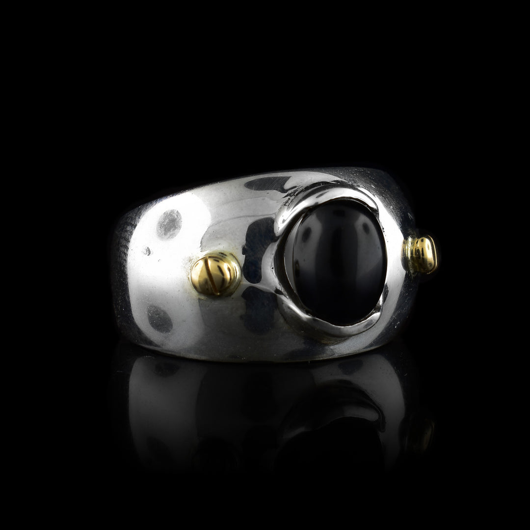 This wide band solitaire ring is made from sterling silver and has a side band that tapers slightly in the back. There is a large, oval shaped black onyx gem in the center with 14K gold studs to either side of it.