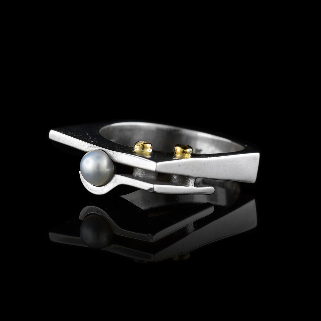 This sterling silver ring is square shaped and has a fresh water pearl held in the top by another square piece. At the top of the ring are two 14K gold studs.
