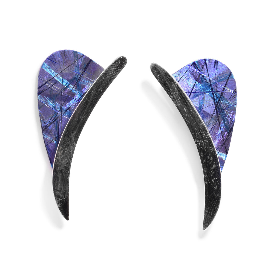 Each of these long stud earrings have a long, curved sterling silver band with a half circle piece of titanium at the top of them. There are blue and purple designs made on the titanium.