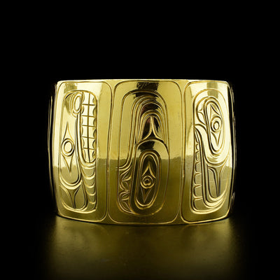 This brass bracelet depicts the heads of multiple legends. Each has been carved in a vertical manner from the top to the bottom of the bracelet. The center of the bracelet includes the Orca, Raven, and Wolf.