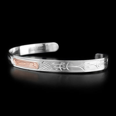 This rose gold bracelet depicts the head of a raven made from rose gold in the center of the bracelet, facing the right. To the right of the head are carvings representing the bird's wing and feathers.
