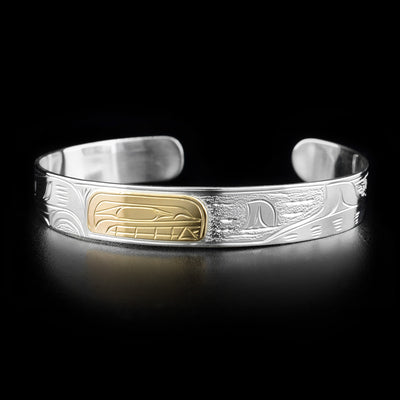 This orca bracelet depicts the head of an orca in the center, facing the right and made out of gold. To the right of it are the fins of other swimming orcas.