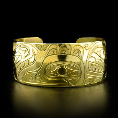 This brass bracelet depicts the head of a raven in the center facing the left when worn. On both sides are the heads of two orcas with teeth showing.