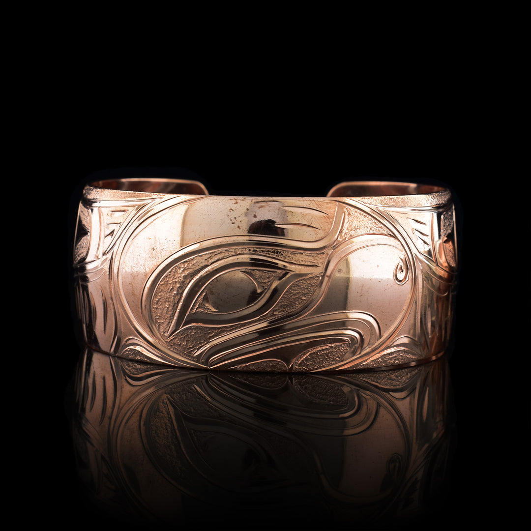 This Eagle cuff bracelet has a single, wide band with a gap in the back that is made from copper. The head of the Eagle is carved into an oval shaped at a side profile. On both ends of the band, there are outstretched wings with feather details included.