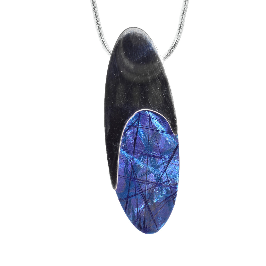 This blue titanium necklace has an oval shaped pendant where the top half is sterling silver which curves around an oval shaped portion of titanium at the bottom. There are blue and purple designs on the titanium.