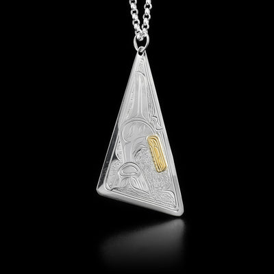 This gold and silver necklace is in the shape of an assymetrical triangle. The designs depicts a full body orca with a head made from gold in the center of the pendant. The background is stippled.