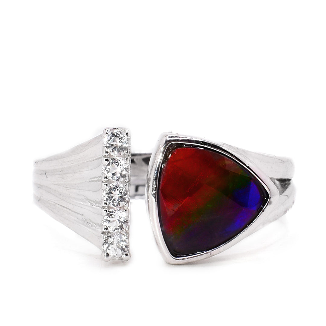A sterling silver ammolite ring. The band is disconnected in the front. One end is wider towards the end and has white topaz details on the end. The other end has a triangular ammolite stone. The ammolite is red at the top, green in the middle, and blue in the bottom.