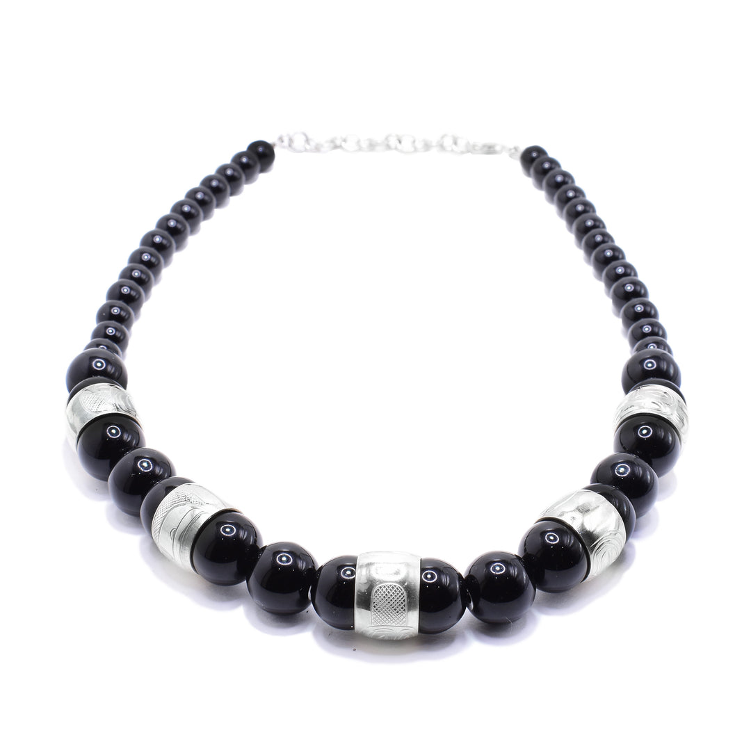 This chunky black jasper necklace has sphere shaped beads that are larger at the bottom of the piece and smaller at the tops of the piece. There are five sterling silver spirti beads featured in the chunky portion of the necklace. There are carvings on the surface of the beads depicting the legends including the Eagle, the Sun, the Moon, the Raven and the Wolf.
