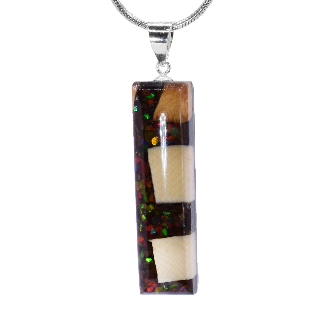 This ivory pendant is made from ammolte gemstone and fossilized mammoth ivory and has a thin, rectangle shape. Chunks of ammolite and ivory have been set into resin and form the pendant.