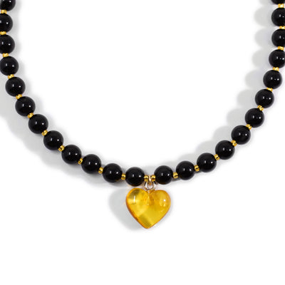 Round polished black onyx beads with small, light-yellow beads in between. Necklace has a yellow amber heart pendant.