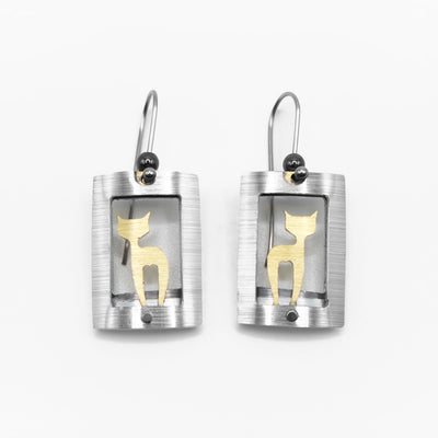 Each earring is a curved, grey frame with a gold-colour cat silhouette inside. Side-view of cat with head turned to side so both ears are visible. By JR Franco. Stainless steel hooks.