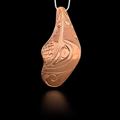 Pendant is an irregular shape and features a hummingbird with its beak in a flower. Textured background. Hand-carved by Kwakwaka’wakw artist Cristiano Bruno.