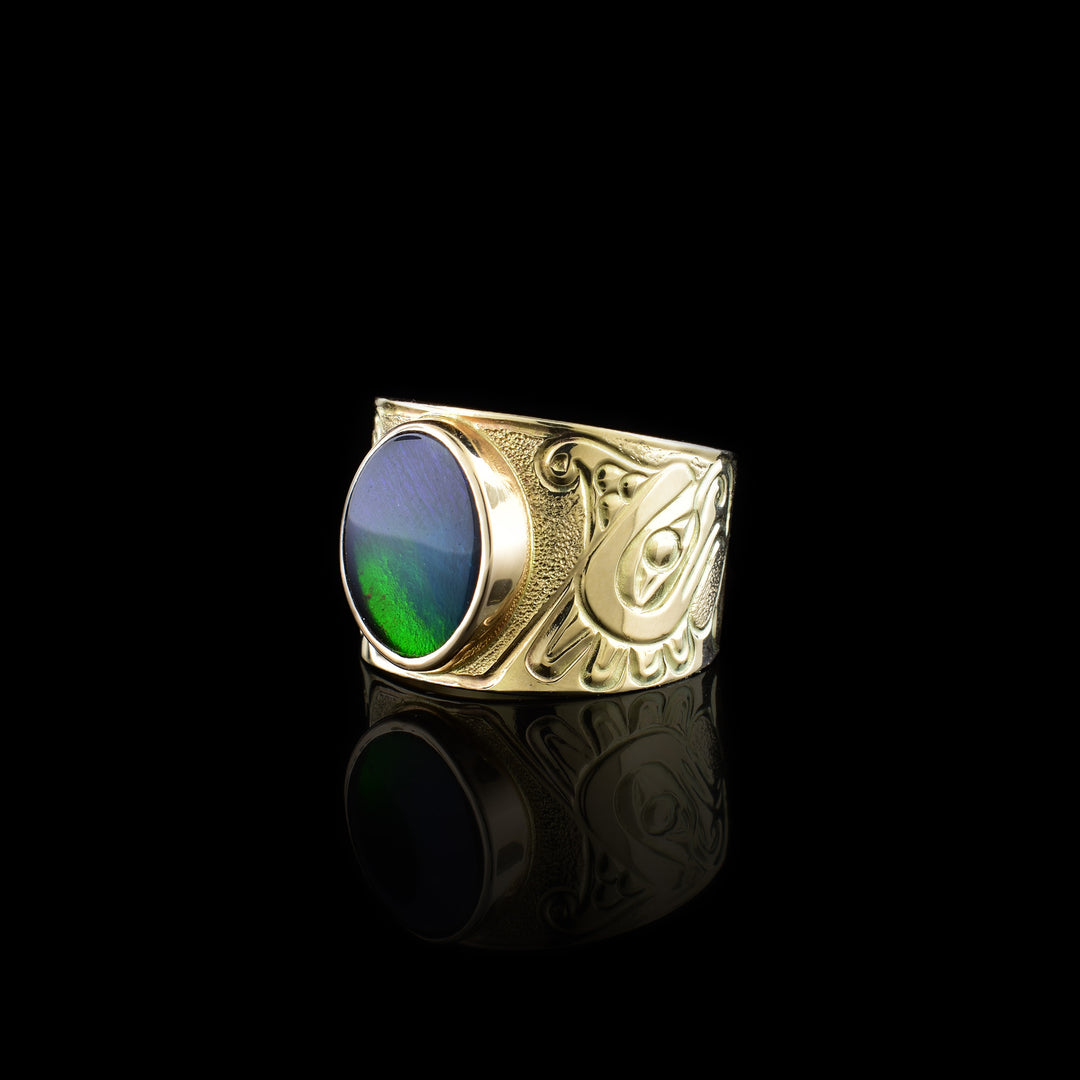 This 14K gold Thunderbird ring has a wide band with a depiction of the Thunderbird carved into the band. There is a large, circle shaped ammolite gem that makes up this large, signet ring.