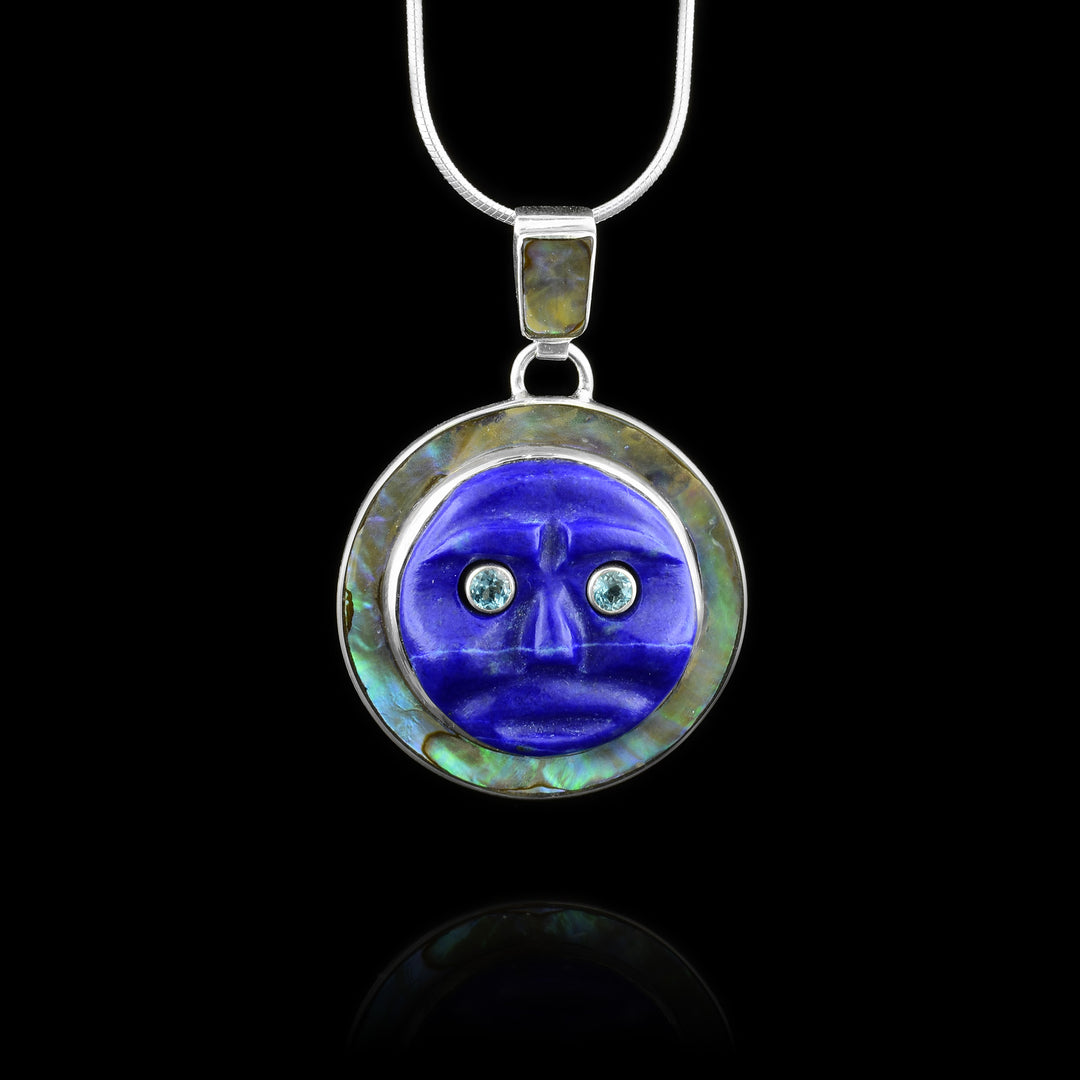 This lapis lazuli pendant is made from a sterling silver circle and has abalone mounted on it. There is a circle shaped, lapis lazuli gem that is carved to depict the moon and is has blue topaz gems as its eyes.