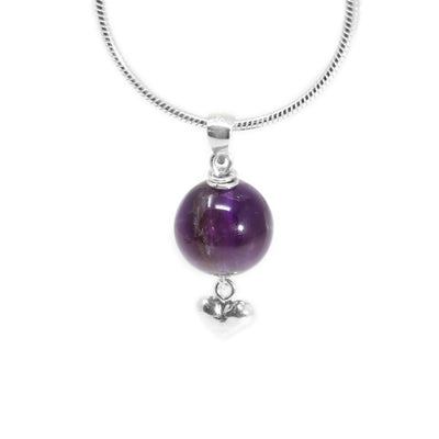 Round amethyst pendant with small silver puff heart adornment hanging below. Two small, silver ring adornments hang off bail. Metal is sterling silver.