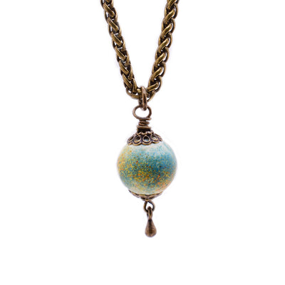 Brass necklace featuring a petite, round handmade lampworked glass bead. Bead is white and is mainly covered by dabbles of blue, yellow, red and orange. By Wendy Pierson.