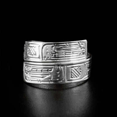 This wrap ring is made out of a sterling silver strip that has two Orca faces carved on the front, where the the ends of the ring overlap. The face of the lower Orca is upside down.