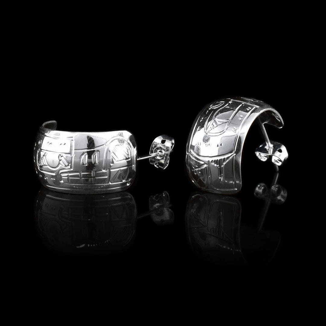 These wide hoop earrings are made from sterling silver and have a single, wide band with a gap in the back. There are carvings on the surface of the hoops depicting the Wolf.