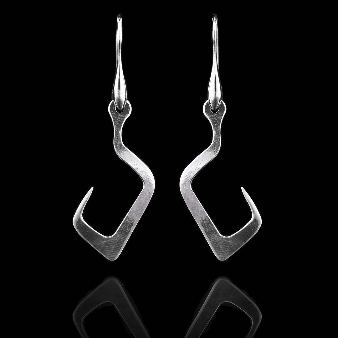 These sterling silver long dangling earrings have thin hangs that drop down and curve upwards. The curves of the hooks are squared. The hangs depict a Haida Gwaii character.
