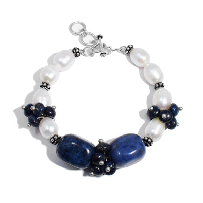 White freshwater pearl bracelet with silver adornments and clusters of lapis beads. Two large rounded rectangular lapis beads on front. Bracelet closes with a toggle clasp. Made with sterling silver.