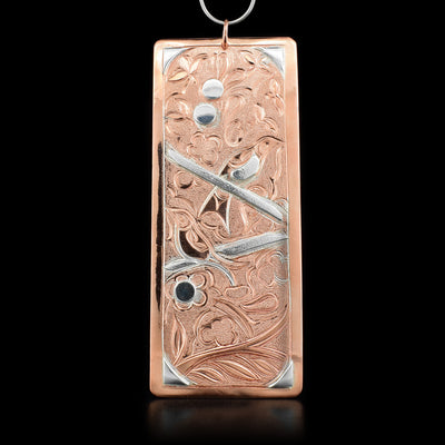 Rectangular copper and sterling silver pendant depicting two hummingbirds sitting on twigs in a floral setting. Hand-carved by Kwakwaka’wakw artist Cristiano Bruno.