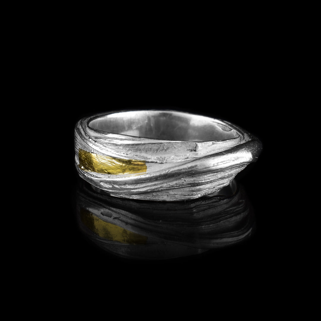 This wavy ring band is made from sterling silver and has flowing designs on the surface of it. The piece is made by casting metal into wax so it mimics the appearance of its wax mold. There are keum boo gold highlights on the band around one of the strips of sterling silver.