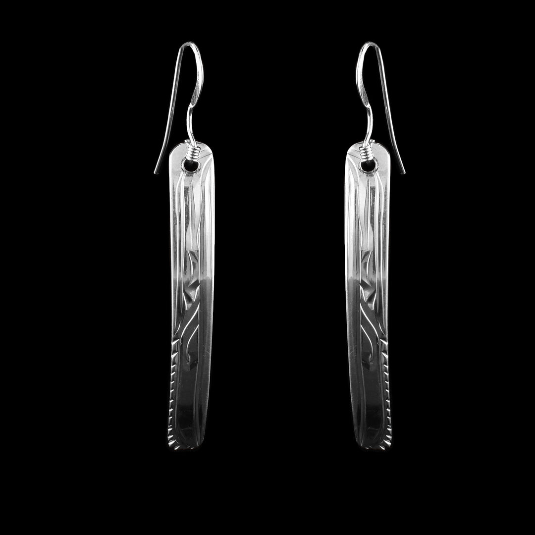 These sterling silver dangle earrings feature an elegant, elongated rectangular shape with a gentle curve. Intricately hand-engraved with a traditional Northwest Coast Indigenous raven, the design showcases flowing lines and abstract forms that represent feathers, beaks, and movement.