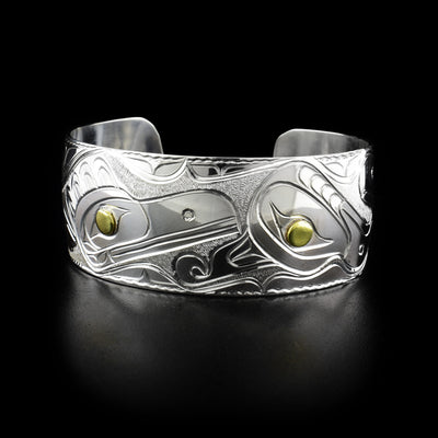 Carved raven and thunderbird head with background designs. Pupils are brass and rest of bracelet is sterling silver.