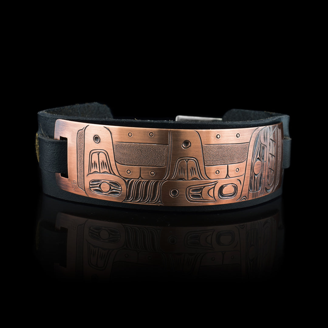 This leather cuff bracelet has a copper band attached at the top of the bracelet. The copper part of the bracelet has a depiction of the Orca carved into it.