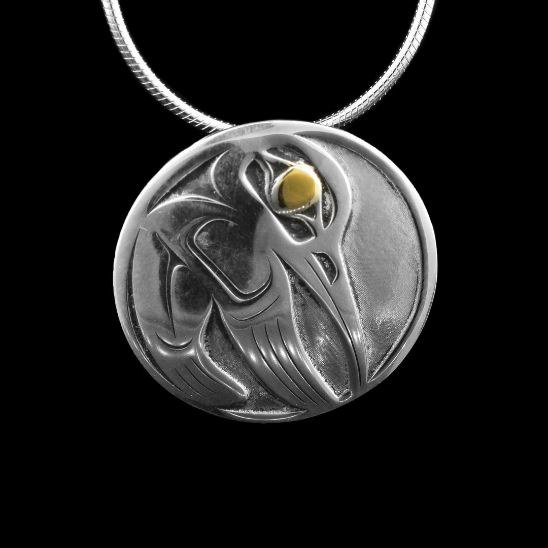 This handcrafted circle pendant features a detailed hummingbird in oxidized sterling silver, accented with a 14K gold eye. A striking blend of tradition and elegance, this unique necklace captures the spirit of the hummingbird in Northwest Coast design.