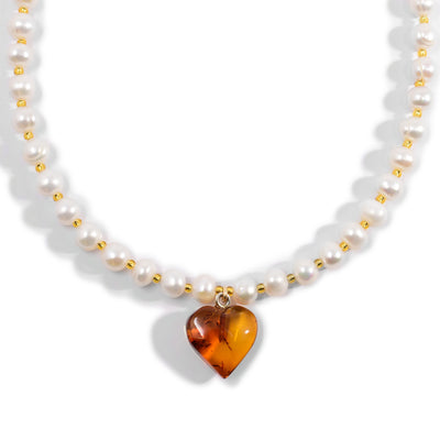 Round white pearls with small, light-yellow beads in between. Necklace has an amber heart pendant.