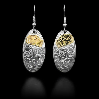 Each dangle earring consists of a curved, oval featuring a bear. Face done in 14K yellow gold. Hand-carved by Kwakwaka’wakw artist William Cook.