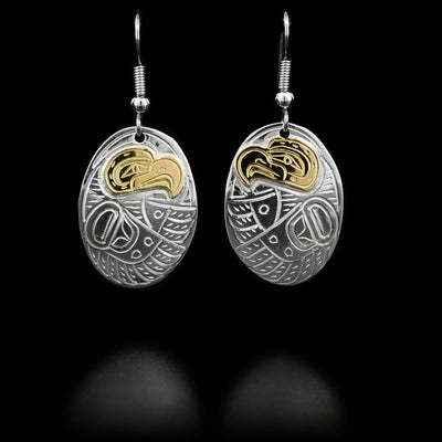 Each dangle earring consists of an oval featuring an eagle with wings outstretched. Eagle head is done in 14K yellow gold. Hand-carved by Kwakwaka’wakw artist William Cook.