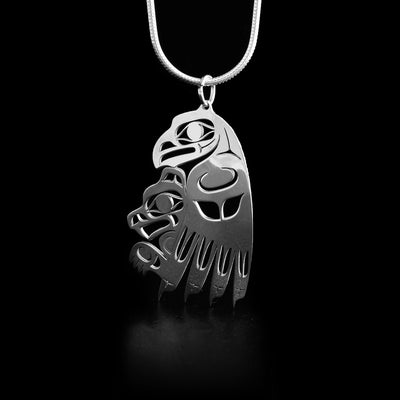 This eagle and bear pendant depicts the side view of a large eagle carrying a small bear in its claws. Both facing the left. Parts of the pendant have been cut out for design and depth.