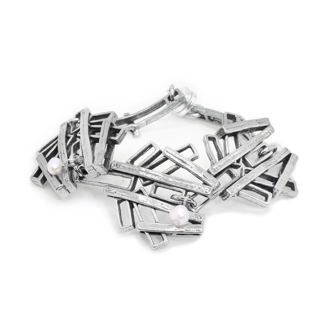 This chunky chain bracelet has large links made from pewter. Each of the links has cutout pieces with some sticking out to the sides and on top of those pieces are strips that branch over them. There are three freshwater pearl charms (one on each ink).
