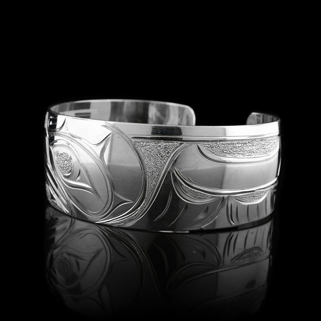 This Eagle cuff bracelet has a single, wide band with a gap in the back that is made from sterling silver. The head of the Eagle is carved on an angle shaped at a side profile. On both ends of the band, there are outstretched wings with feather details included.