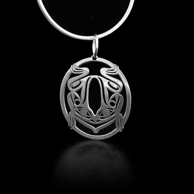 This frog pendant is oval in shape and depicts a full-size frog facing the bottom of the pendant. The background and parts of the frog have been cut out to give it depth.