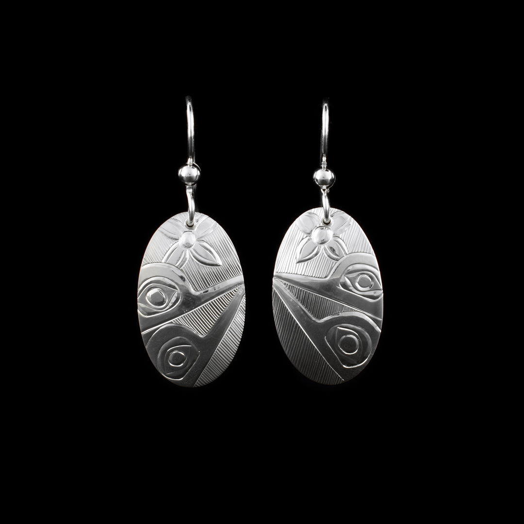These sterling silver Hummingbird earrings have oval shaped hangs that are longer, horizontally than they are wide. There are two Hummingbirds facing the side with their beaks meeting at the opposite side of the hangs carved into them. There is a flower carved at the top of the hangs and in the negative space there are hatching patterns made.